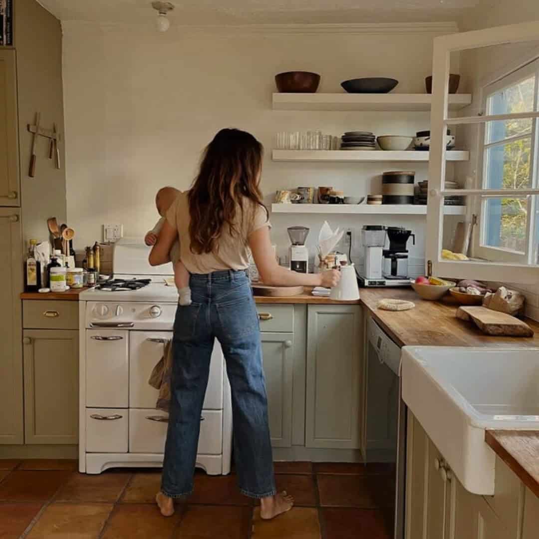 Une maman prépare le repas dans sa cuisine, son bébé dans les bras