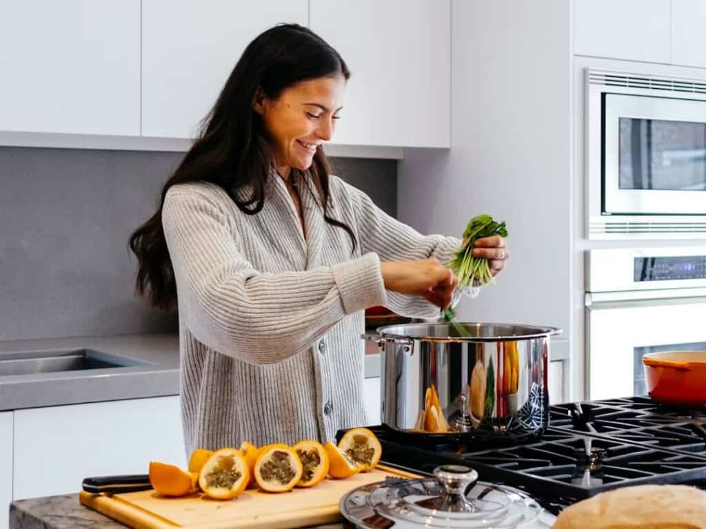 Femme souriante qui cuisine dans une cuisine lumineuse, un bouquet d'herbes fraîches à la main