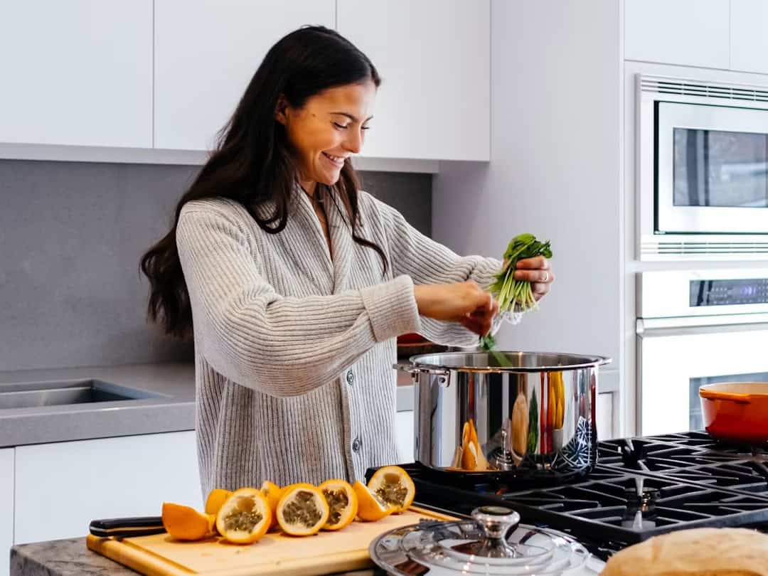 Femme souriante qui cuisine dans une cuisine lumineuse, un bouquet d'herbes fraîches à la main