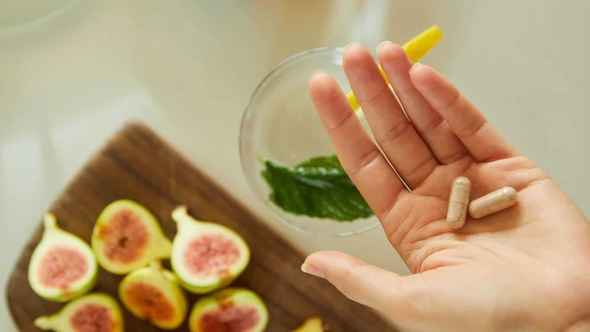 Gélules de complément alimentaire dans la main, à côté de figues, d'orange et de gingembre, SPM et compléments